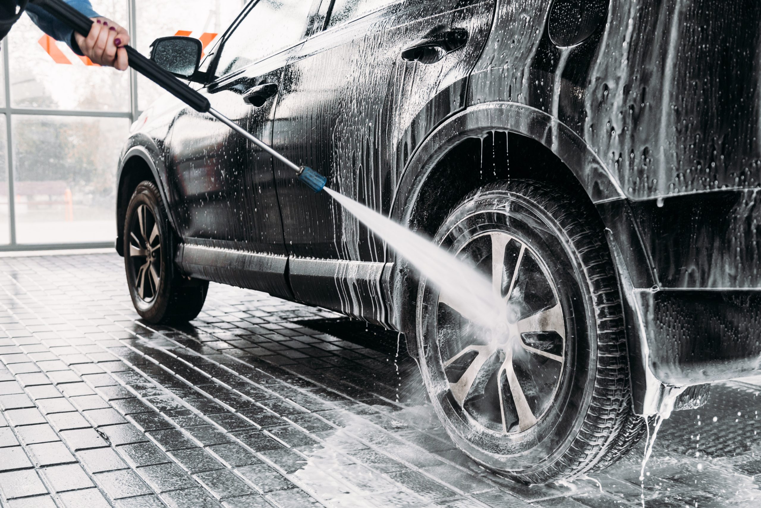 Woman,Washing,Her,Car,In,A,Self-service,Car,Wash,Station.car A black car covered in soap being hosed off