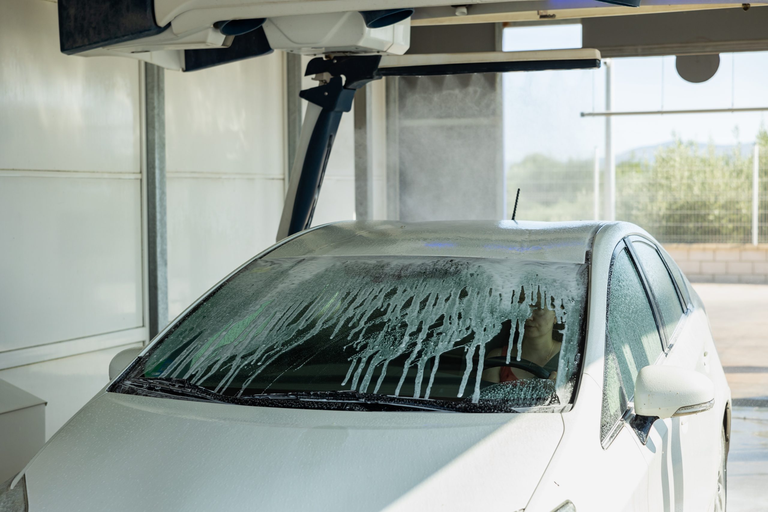 Process,Of,Car,Washing,With,Driver,Inside.,Automatic,Car,Wash A white car driving through an express car wash
