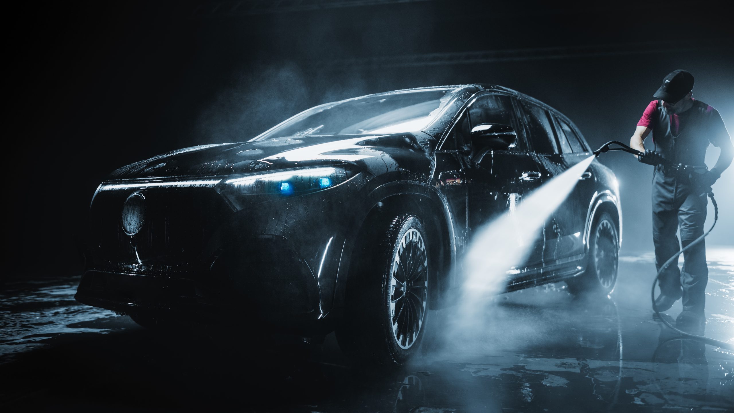 Brand,New,Electric,Vehicle,From,A,Production,Line,Is,Being A black car being powered washed by a man in the dark