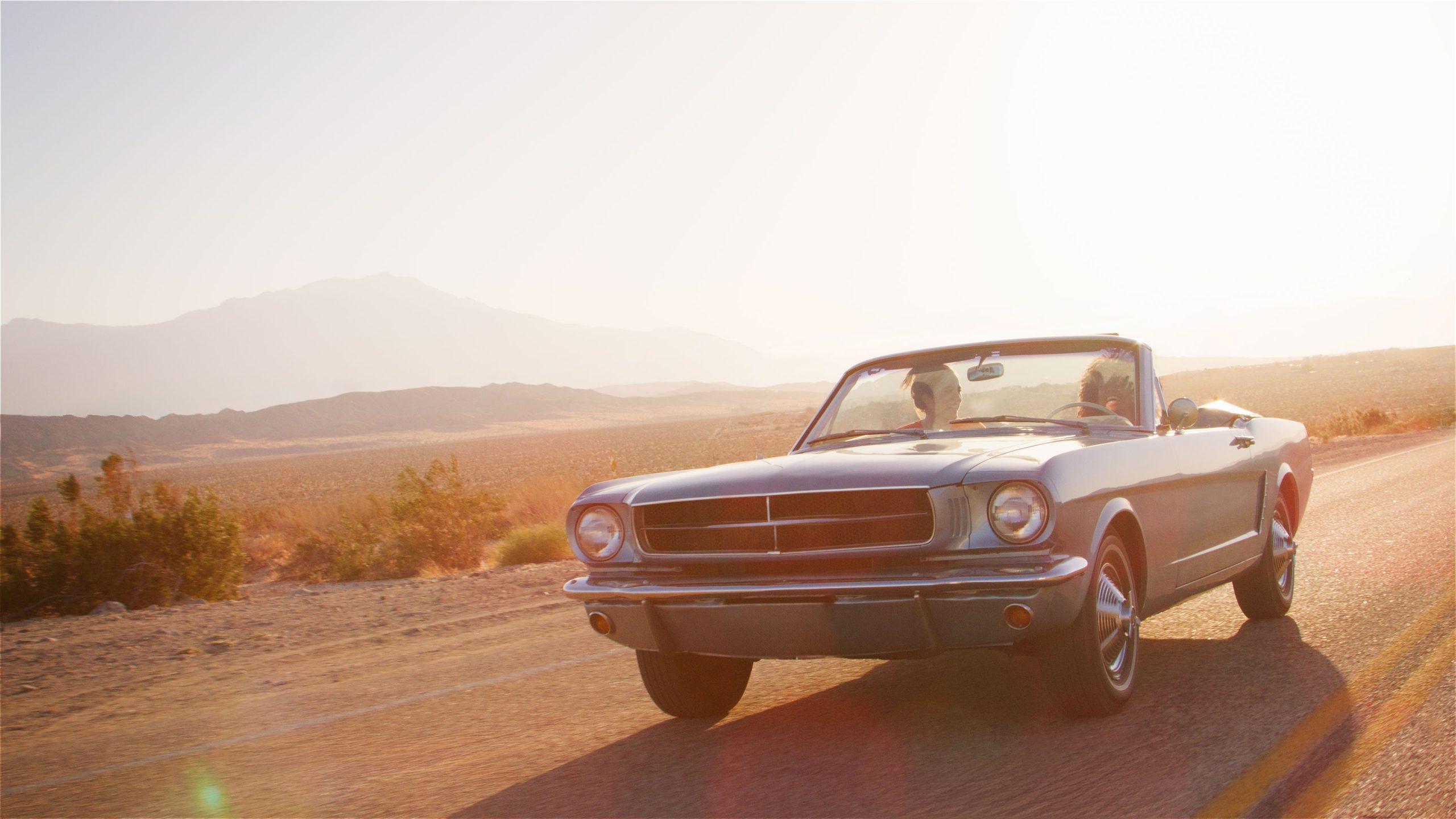 Two,Young,Female,Friends,On,Road,Trip,Driving,In,Classic A pair of women driving a blue convertible with the top down