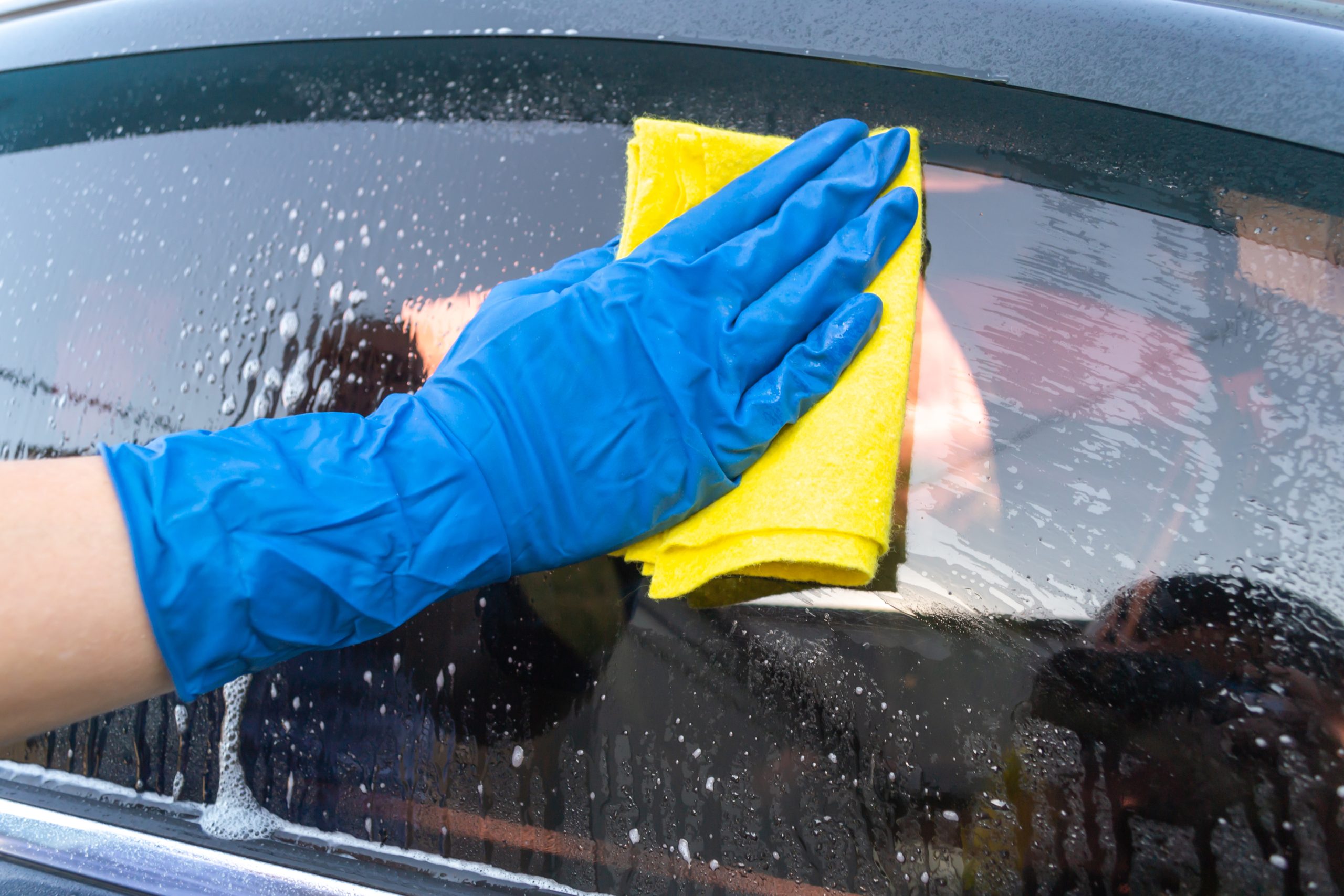 Car,Wash,,Woman,In,Blue,Gloves,Rubs,Auto,Glass A person wearing a blue glove drying off a car's window with a chamois cloth