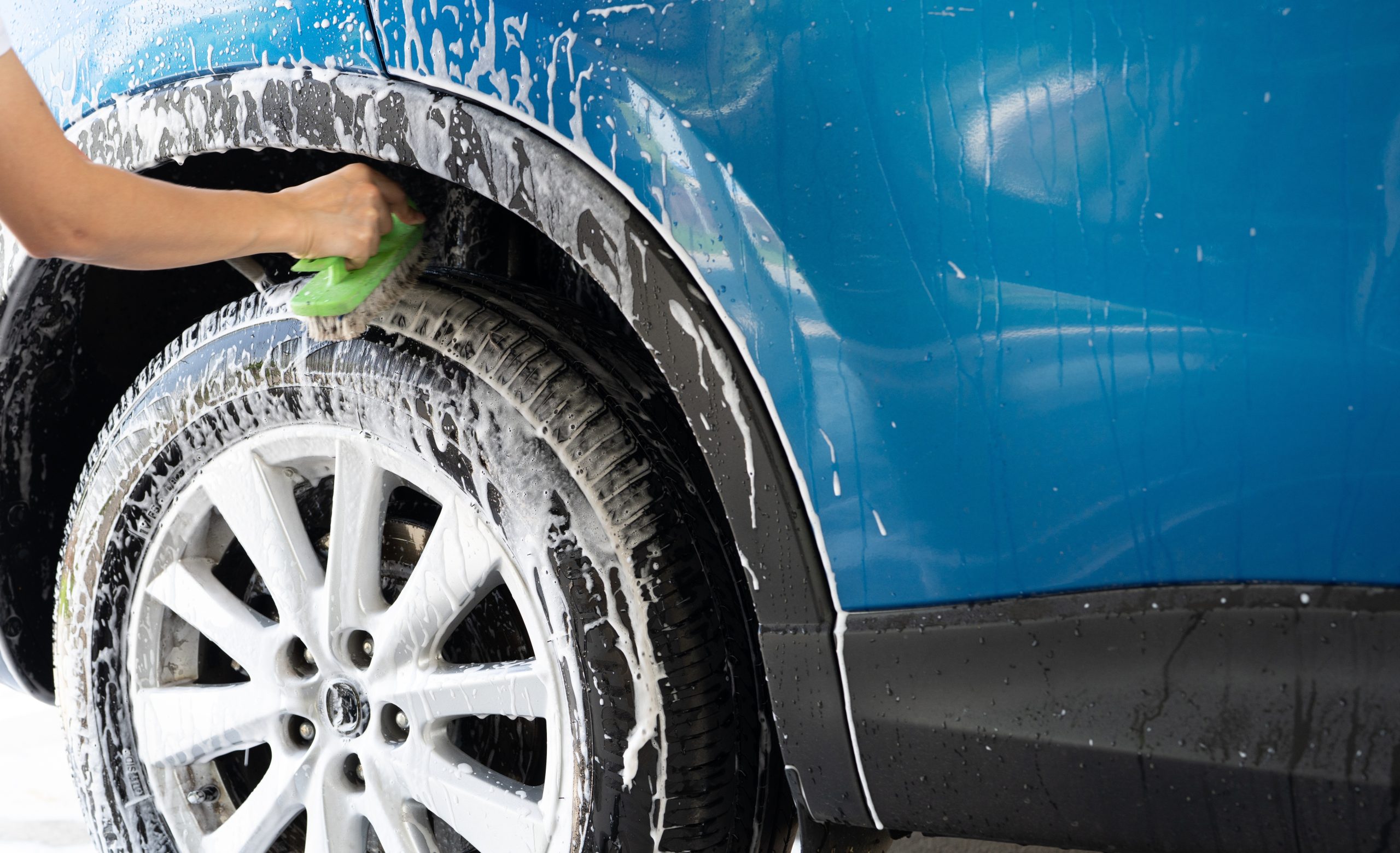 A,Person,Is,Washing,A,Car,Tire,With,A,Green A person washing a blue car's tire